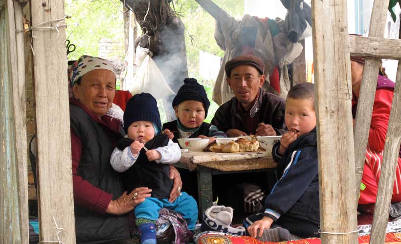 Kyrgyz family of six in a wooden hut eating lunch