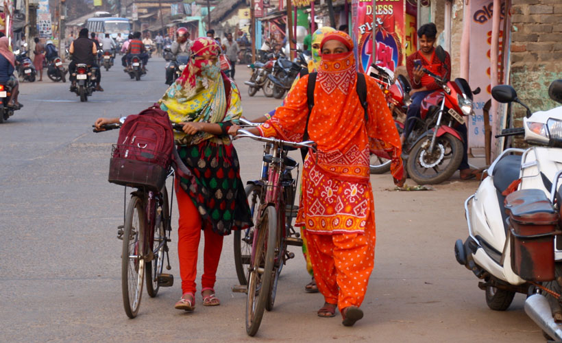 Two Indian girls in colourful saris walking their bikes